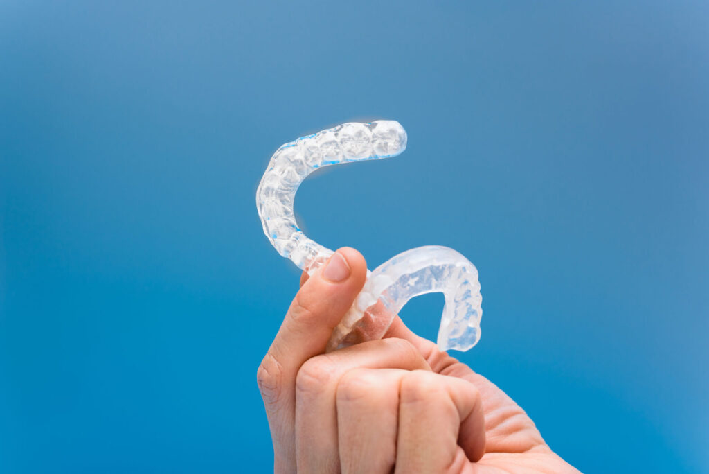 Comparison between biofeedback and mouthguards: A hand holds mouthguards against a serene blue background